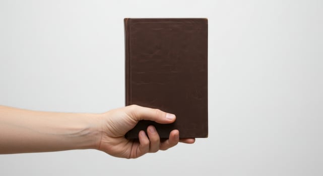Hand Holding a Brown Book Against White Background, Focused on the Text and Cover Detail. photo