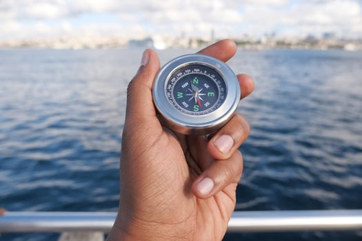 Compass held by a person near calm water in daylight photo