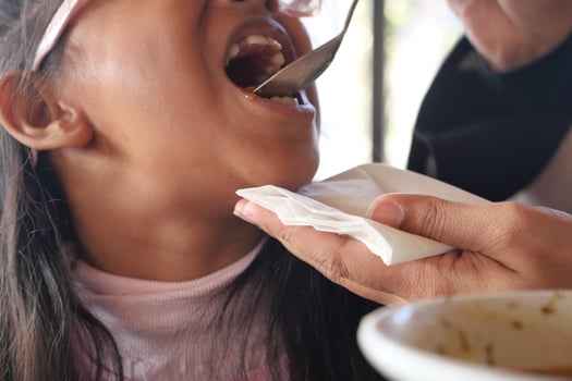 Child enjoying a meal while receiving food from an adult photo