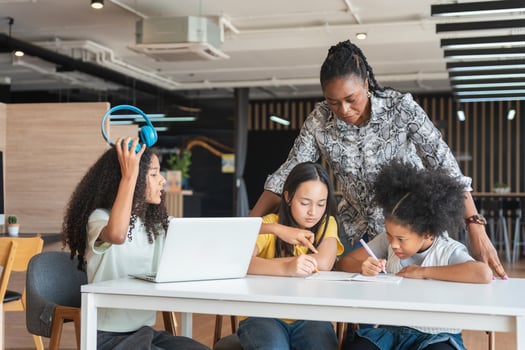 Educator Assisting Children with Schoolwork and Laptops, Multi-ethnic Group of Kids Learning Together with an Instructor, Teacher Guiding Diverse Students in a Modern Classroom photo