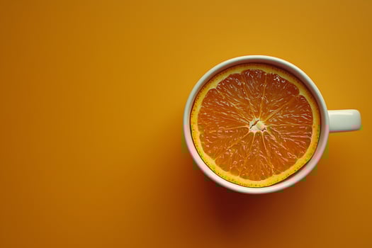 A Single Slice of Orange in a White Mug Against a Vibrant Orange Background. photo