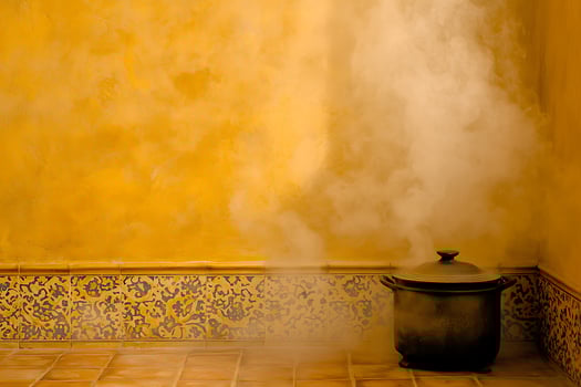 Steaming Pot in a Yellow Room with Ornate Tilework. A rustic pot with steam rising against a warm yellow wall accented by patterned tiles. photo
