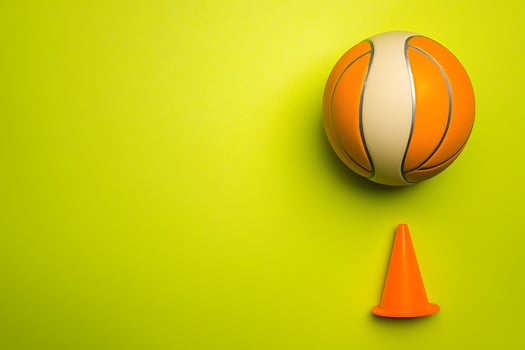 Orange Basketball and Traffic Cone on Lime Green Background Sport and Safety Concept. photo