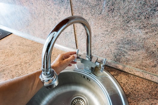 A person skillfully opens a kitchen sink faucet, which is a vital and essential fixture that dispenses water and other liquids necessary for a wide variety of household tasks and activities photo