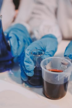 A person in blue gloves holding a beaker with liquid photo