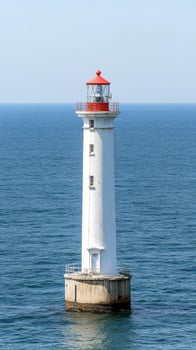 Majestic White Lighthouse with Red Cap Standing Tall in the Calm Blue Ocean. A Guiding Beacon for Maritime Navigation and Coastal Beauty. photo
