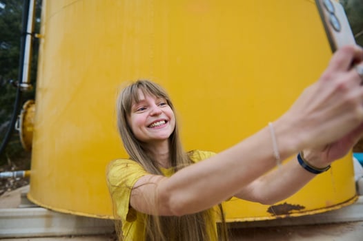 Smiling Woman Taking a Selfie in Front of a Bright Yellow Tank in an Outdoor Setting photo