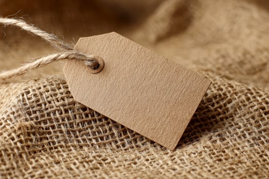 Close up of a brown paper tag resting on a burlap cloth, sitting atop a woven surface in a neutral and rustic setting,. photo