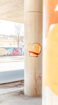 Whimsical yellow character sticker on a textured concrete bridge pillar, showcasing vibrant urban street art and the raw beauty of city architecture. photo