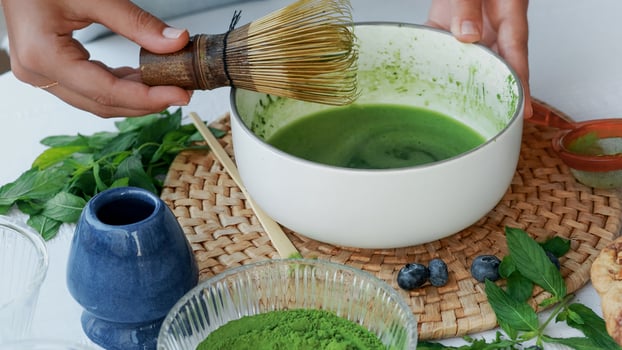 Whisking matcha green tea in a white bowl with a traditional bamboo whisk. Authentic preparation of a healthy antioxidant drink at home with fresh natural vibes photo