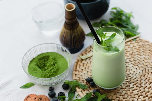 Refreshing vegan matcha latte with ice and mint leaves. Surrounded by organic powder, cookies, and berries for a wholesome, clean eating lifestyle. Top view photo
