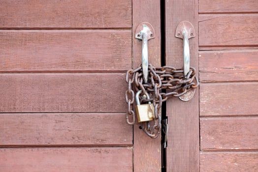 Close up of a rusty metal chain and padlock securing wooden double doors. Concept of security, lockdown, privacy, or restricted access. Symbol of protection and safety photo