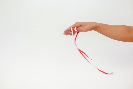 Hand holding a red and white ribbon against a plain white background in studio photo