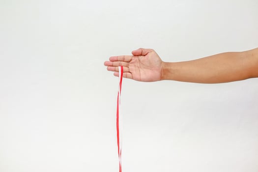 Hand holding a red and white striped ribbon against a plain white background in studio photo