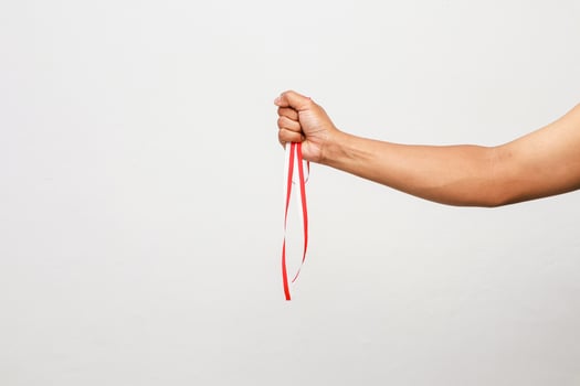 Arm Holding Red Ribbon Symbolizing Support for a Cause Against a White Background photo