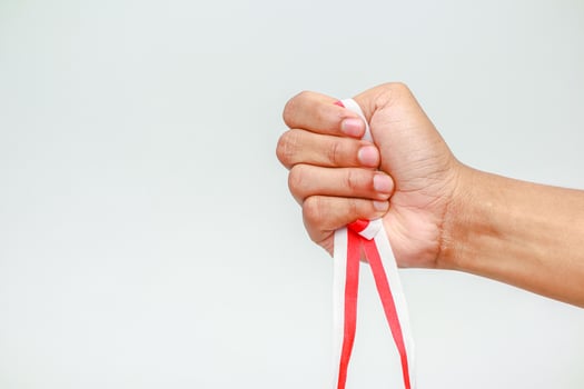 Hand gripping a red and white ribbon, symbolizing strength and national pride, isolated on white photo