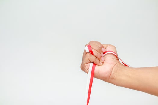 A hand clenched around a red and white ribbon on a plain background creating a sense of solidarity photo