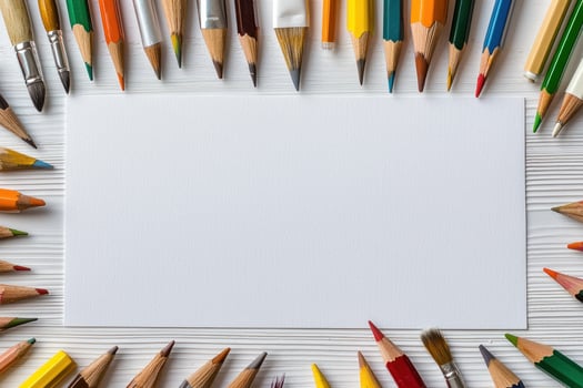 Colorful pencils and brushes frame blank white paper on wooden surface photo