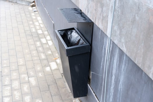 A black trash bin is installed on a wall next to a stone pathway, promoting cleanliness in the urban area photo