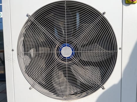 A large air conditioning fan is visible on a building's side, providing airflow under a bright, sunny sky in a warm environment photo