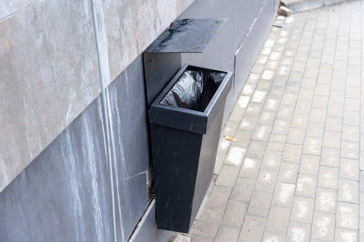 A sleek black trash bin is mounted on a building exterior, positioned against a paved walkway, providing waste disposal in an urban area photo