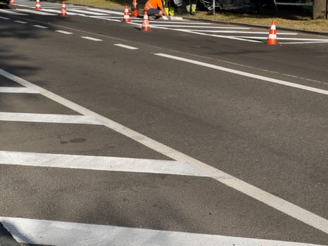 Workers in safety gear apply fresh paint on road lines with traffic cones placed around their work area in the morning light photo