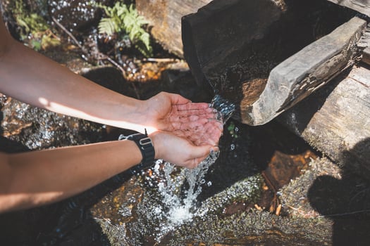 Woman on a hike quenches her thirst with fresh water from a stream originating in the Beskydy Mountains. Hydration as part of a sporting activity photo