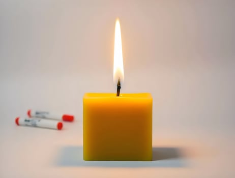 A yellow candle with a lit match next to it photo