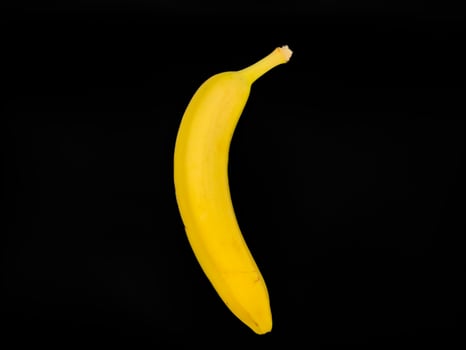 A yellow banana is shown on a black background, copy space, flat lay, one banana photo