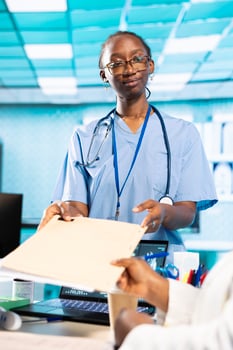 African american female nurse provides medic with the patient file during consultation, review medical records to ensure disease prevention and wellness for young man. Leveraging health reports. photo
