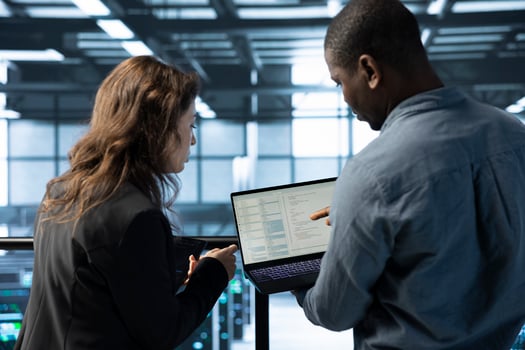 Programmers in data center workspace coding on laptop, analyzing metrics, optimizing storage volumes. Teamworking IT professionals in server hub using notebook, chatting, ensuring seamless operations photo