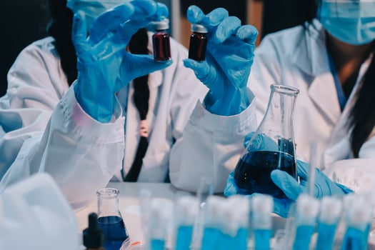 Two people in lab coats and gloves holding blue liquid photo
