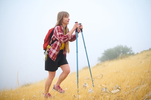 Young Woman Hiking Uphill in a Scenic Misty Field with Trekking Equipment photo