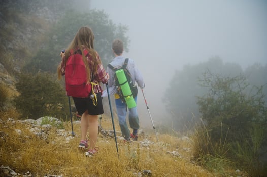 Couple Hiking Through Misty Mountain Trail with Backpacks and Trekking Poles photo