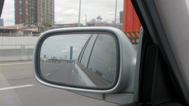 A view of Bangkok's skyline captured in a car's rearview mirror during a highway drive, creating a layered perspective of urban travel. photo
