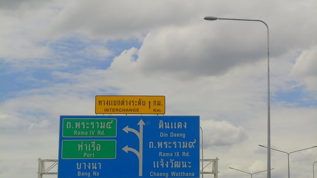 Close-up view of bright Thai expressway signs with bilingual directions under a partly cloudy sky, illustrating highway navigation in Bangkok. photo
