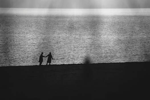Silhouette of two people holding hands on beach at sunset, with ocean reflecting light. Black and white, soft glow. Concept of love, connection, and serene coastal moment. photo