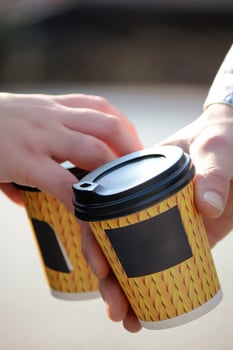 Close-up of Two hands touching coffee cups in disposable yellow knitted-patterned sleeves with black lids, close-up shot. Concept of warmth, sharing, friendship, and cozy outdoor moments. photo
