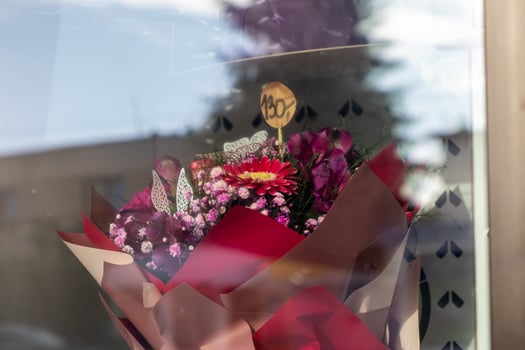 Vibrant flower bouquet featuring a bold red gerbera and purple blooms, elegantly wrapped, displaying a 130 price, seen through a reflective shop window photo