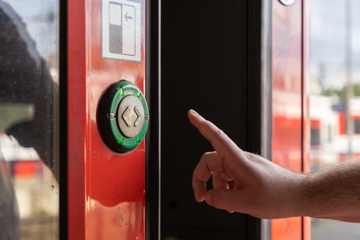 Person's hand reaching to press a green illuminated door open button with a door icon on a red public transit train for efficient urban mobility photo