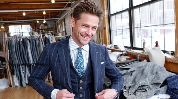 Smiling tailor in workshop adjusts bespoke navy pinstripe suit on himself photo