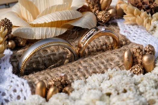 Close-up shot of a pair of gold wedding rings. Wedding ring or engagement ring in an aesthetic jewelry box containing dried decorative flowers, burlap and beads. Text space photo