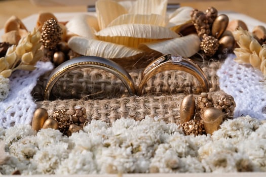 Close-up shot of a pair of gold wedding rings. Wedding ring or engagement ring in an aesthetic jewelry box containing dried decorative flowers, burlap and beads. Negative space photo