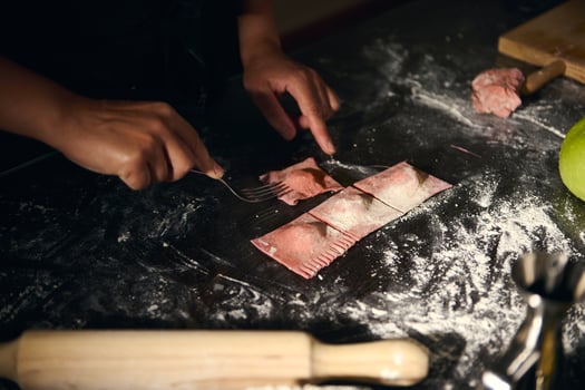 Woman Preparing Homemade Ravioli with Red Pasta Dough in Rustic Kitchen Setting photo