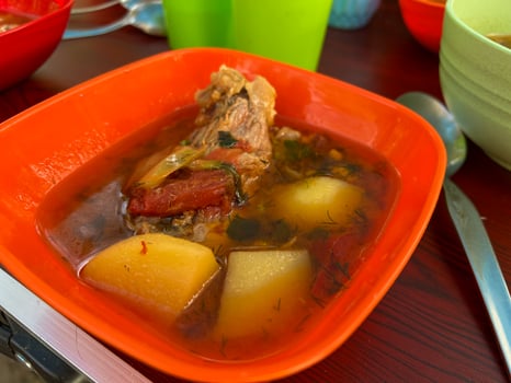 Steaming hot meat and potato soup served in bright orange bowl photo