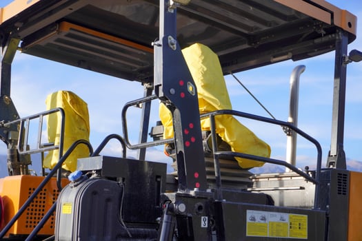 The image features a close-up of a construction vehicle's operator seats, covered in bright yellow protective fabric. The machinery has a black frame and visible controls. photo