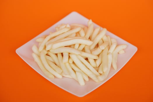 Crispy potato sticks on a white square plate, set against an orange background. Crunchy snack that brings joy to every bite perfect for kids, parties, and playful moments. Irresistibly tasty. photo