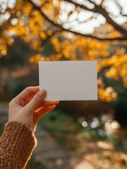 Female hand holding blank card in autumn scene with golden leaves photo