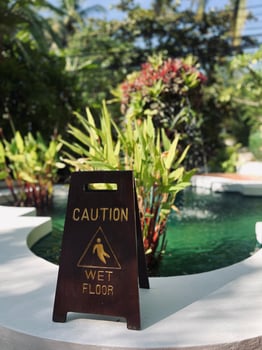 A dark colored Caution Wet Floor sign with yellow lettering stands on a white. photo