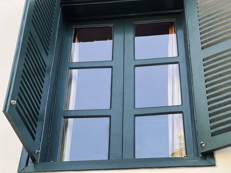 Elegant window with dark green wooden shutters partially open, featuring a six-pane glass design. photo